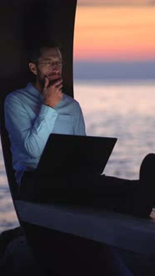 Man Working on Laptop by Ocean at Sunset