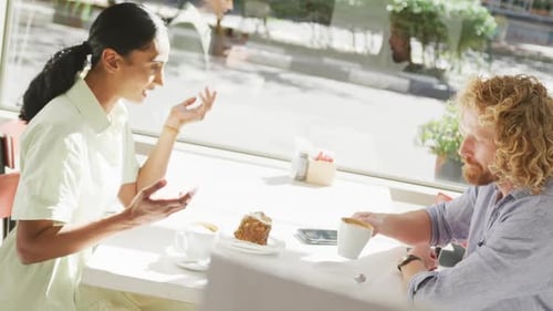 Happy diverse couple drinking coffee and talking at a table in cafe