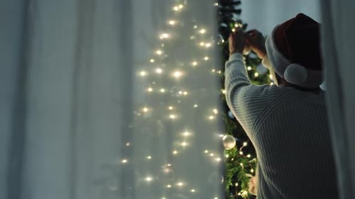 Man Decorating Christmas Tree Wearing Santa Hat