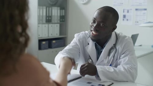Doctor Greeting Patient with Handshake and Giving Consultation in Clinic
