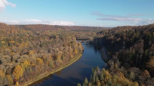 The drone advances toward a bridge across a hilly autumn landscape, gently descending while tilting