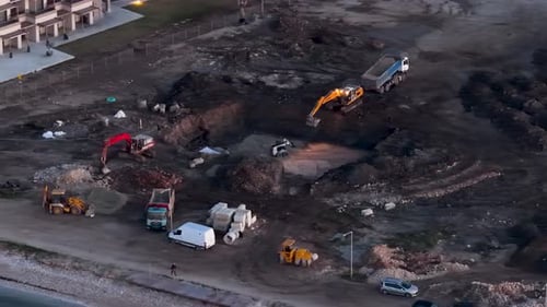 Top Down Aerial View of Active Construction Site with Excavators Digging Earth and Dump Trucks