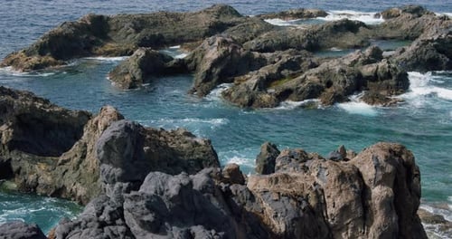 Ocean wave water lapping washing black rock stone close up with light reflection water surface foota