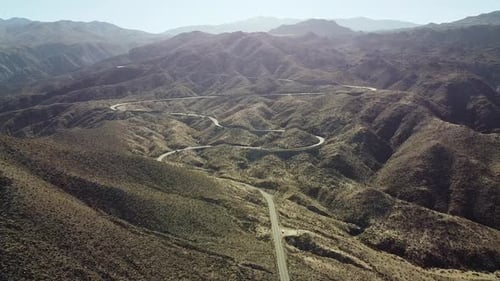 Winding highway road on hilly desert landscape on sunny day, aerial fly backward shot