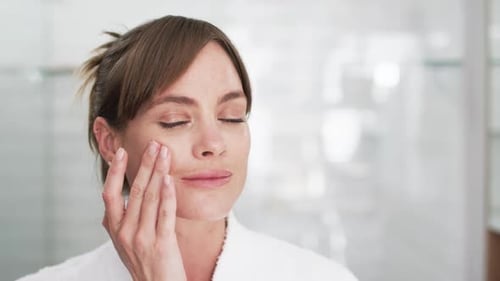 Middle-aged Caucasian woman examines her skin in a bright bathroom