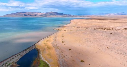 Dry desert next to the vast blue lake. Drone flight above the shore of the waterscape