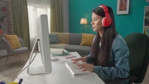 A Woman in Headphones Works at a Computer A Young Woman Listens to Music and Types on the Keyboard