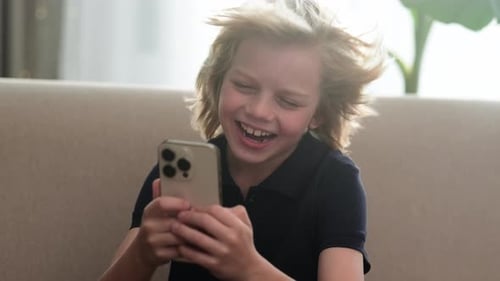 Niño caucásico sorprendido, sorprendido, mirando el teléfono y gritando de felicidad, sentado en casa encendido