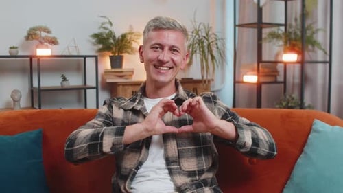 Smiling Man Makes Heart Shape with Hands on Couch