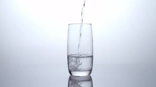 Drinking Water Being Poured Into A Glass On The Light White Screen Background In The Studio