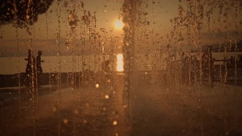 A Stunning Golden Sunset Beautifully Glimmers Through Enchanting Water Fountains at the Beach
