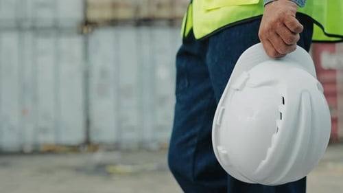 Nahaufnahme eines Bauarbeiters, der in der Nähe des Containerterminals läuft und einen Helm trägt
