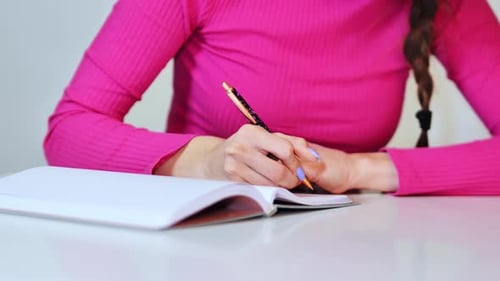 Close-Up of Female Hand with Braided Hair Writing on Paper Using Colored Pencil