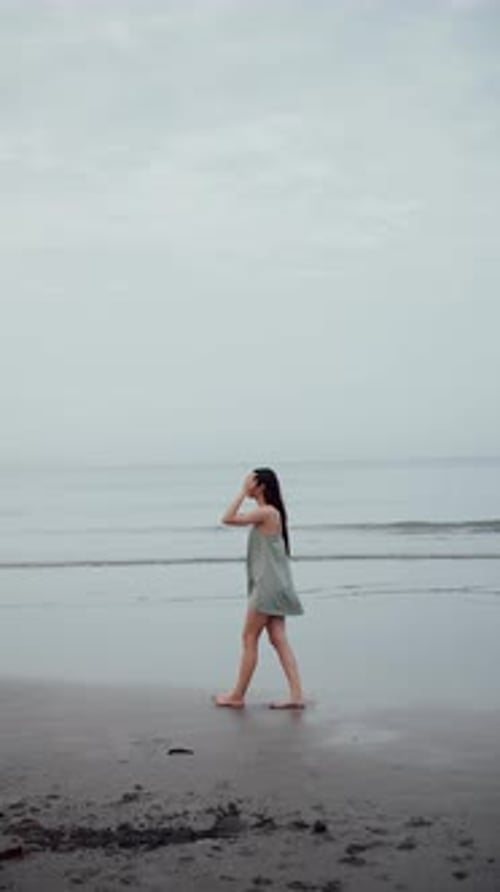 a Girl with Long Hair on the Ocean Walks on Black Sand Vertical Video
