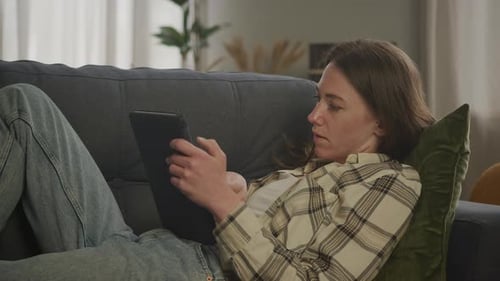 Woman Relaxes on Couch Using Tablet Device