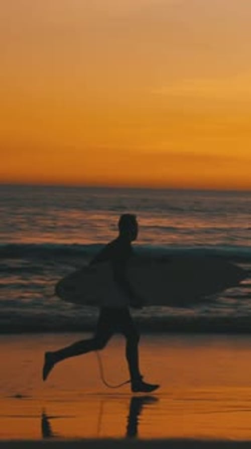 Silhouette of Surfer Running with Board on Beach at Sunset