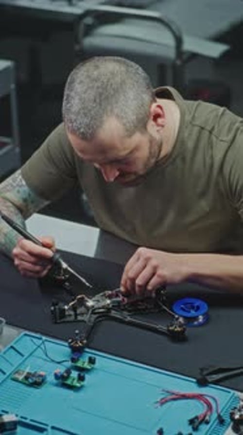 Konzentrierter Mann verwendet Lötkolben, um Mikrochips und Kabel auf dem zentralen Mainboard der Drohne zu befestigen