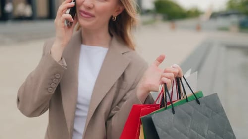 Smiling Woman on Phone Holding Bags Near Shopping Center