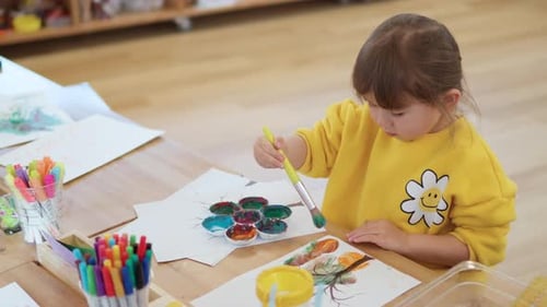 Focused Child Painting Pictures at Wooden Table