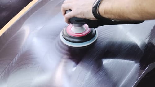 Car detailing. A man polishes the hood of a car with an orbital polisher. A beautiful wavy mark from