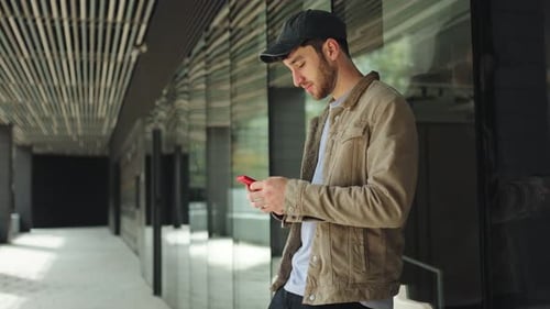 Young Man Uses Phone Leaning Against Building Outdoors