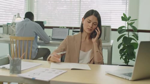 Female Manager Speaking on Phone and Taking Notes in Office