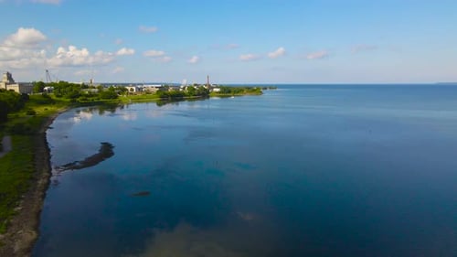 Aerial view rotate around summer peninsula shore industrial area by sea with coastal urban greenery