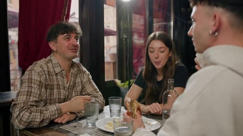 Wide shot - a group of friends chatting at a table in a restaurant, eating a burger and french fries