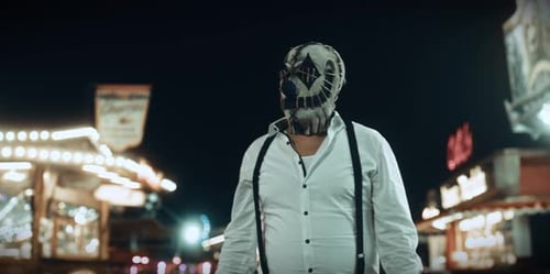 Masked Figure Walks Through Fairground at Night