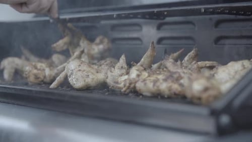 In Zeitlupe einige Hühnerflügel auf dem Grill grillen und umdrehen, dabei etwas Rauch um den Grill herum