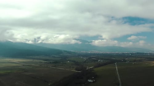 Drone shot of a field мountain and city at the background with cloudy sky