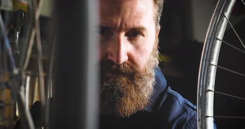 Well-groomed handsome bearded master hipster, specialist in bicycles, repairing a bicycle in his w