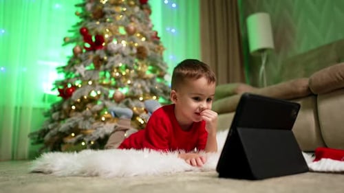 Child Watching Tablet by Christmas Tree at Home
