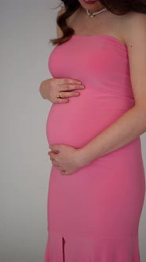 Pregnant Woman Holds Baby Bump Wearing Pink Dress