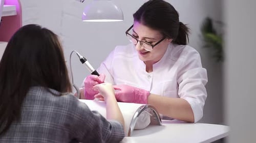 Mädchen macht eine Maniküre in einem Schönheitssalon. Nagelpflege. Maniküristin in pinken Handschuhen entfernt Gel-Nagellack von