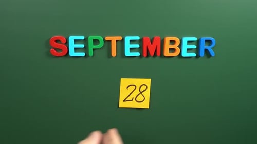 Hand sticking a sticker 28 September calendar day on school board. 28 date of September. Twenty