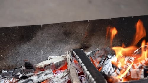 Zeitlupen-Nahaufnahme eines leeren Eisengrills mit Feuer, Flammen und Funken im Freien, Sommerkonzept von