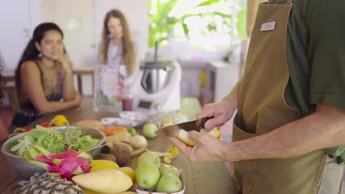 Man Prepares Tropical Fruits with Women Watching