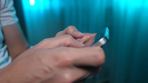 Nahaufnahme eines nicht wiederzuerkennenden Mannes, der eine SMS-Nachricht auf dem Smartphone schreibt, auf dem Sofa im Zimmer mit weichem