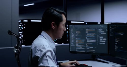 Programador asiático masculino escrevendo código em desktops usando vários monitores na sala de servidores