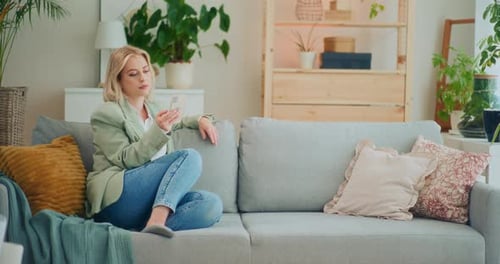 Woman Relaxing on Sofa Using Smartphone at Home