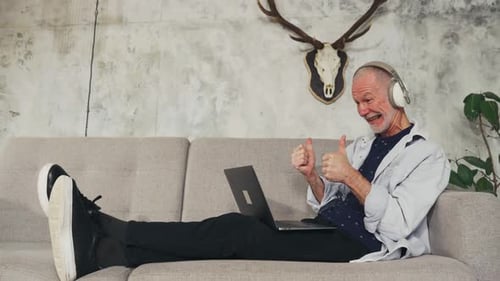 Man Relaxing on Couch, Using Laptop and Headphones
