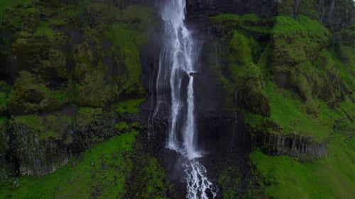 The Waterfall flows over the Rocks, Waterfall view, Mountain waterfall in Iceland - aerial pullback