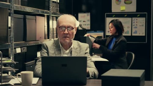 Woman Presents Charts to Senior Man in Dark Office