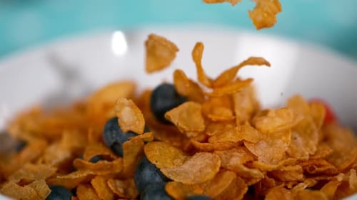 Golden Cereal Flakes and Blueberries Falling into Bowl