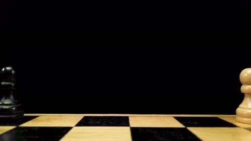 Dolly shot backwards along the chess pieces standing on either side of the chessboard against a blac