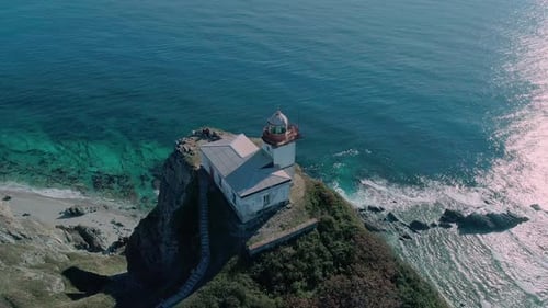Aerial Panoramic View of White Lighthouse on the Rocky Cliff at Seaside Waves are Crashing to the