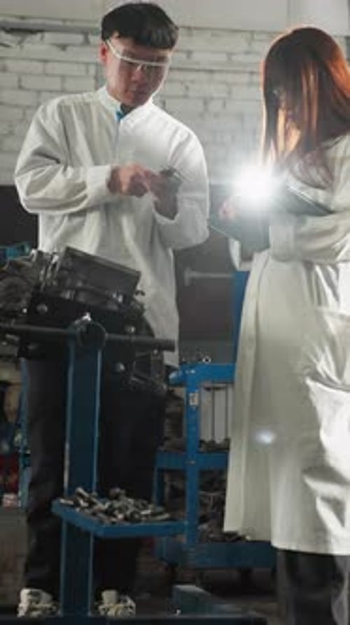 Professional Measuring Engine Thickness While Colleague Records Data in Automotive Shop