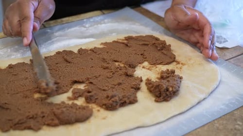 Spreading cinnamon and brown sugar filling on dough to make tasty, sweet rolls - side view in slow m