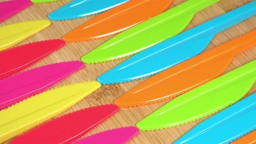 Colorful Plastic Knives Arranged on a Wood Board